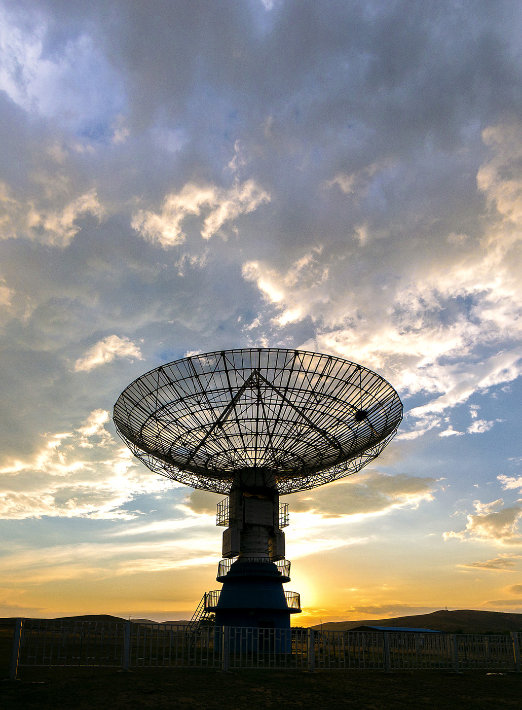 Foto mostrando uma grande antena parabólica com o pôr do sol ao fundo