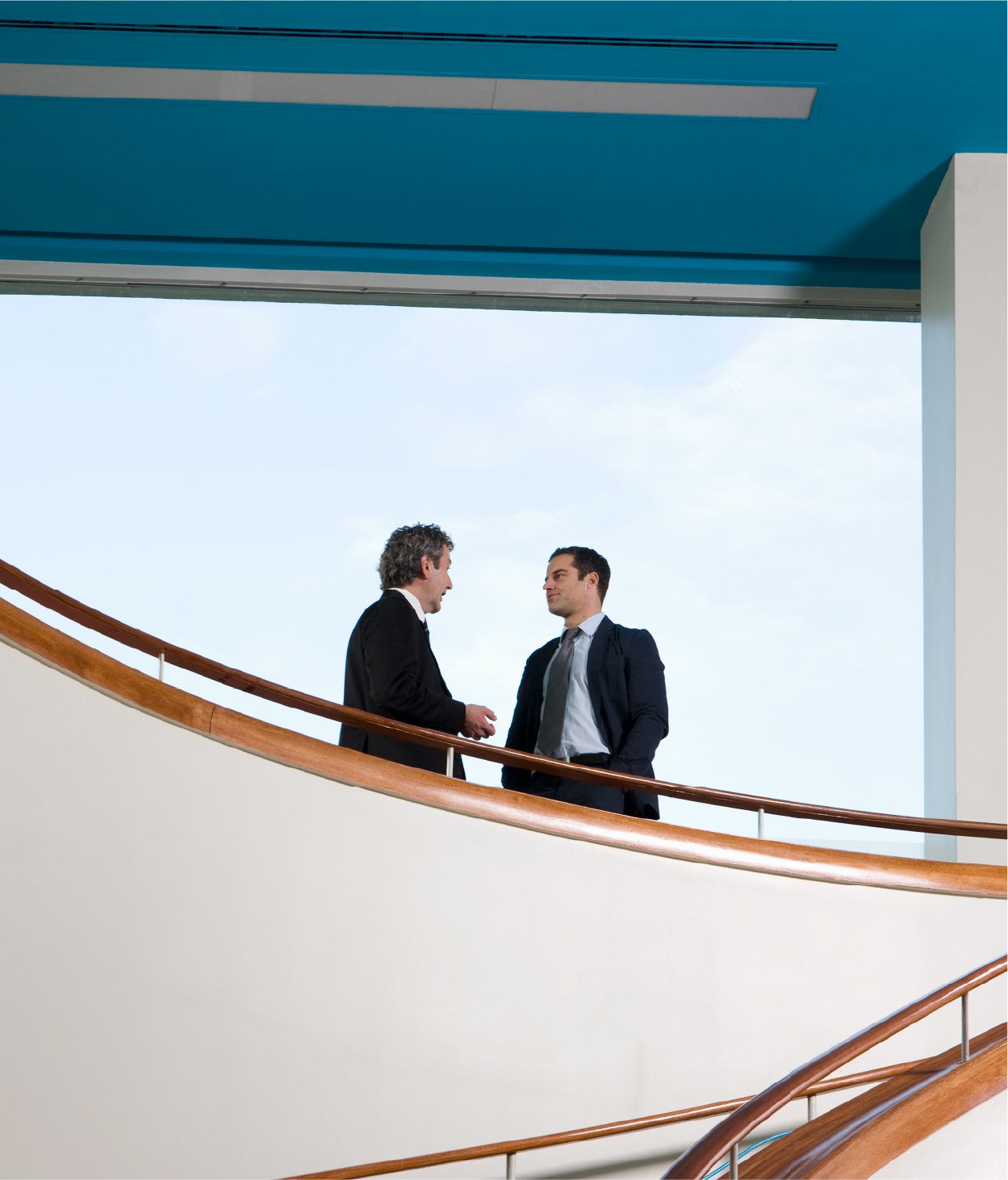 Two men in business suits chat on a balcony