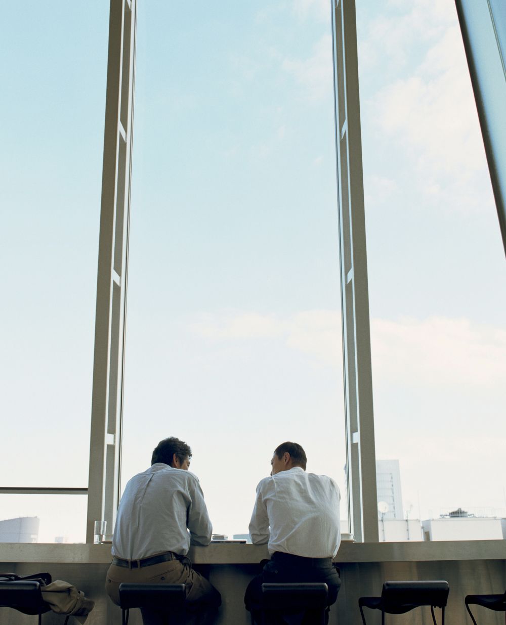 Two men having a discussion in front of a large window.